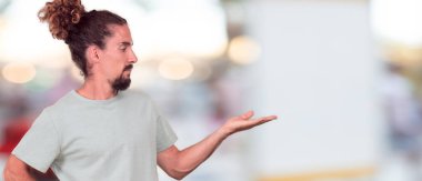 bir nesne veya kavramı tek elle ve diğer el ile kalça üzerinde gösterilen memnun bir ifade ile gülümseyen genç hipster adam.