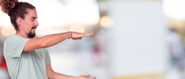 bir nesne veya her iki el arasında yanal düzenlenen kavramı gösterilen memnun bir ifadeyle gülümseyen genç hipster adam.