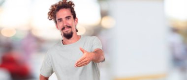 bir gülümseyen genç hipster adam kendine güvenen, gurur, memnun ve iyi bir anlaşma kapanış bir el sıkışma sunan samimi ifade veya tebrik ve sizi karşılayan. Yanal veya yan görünüm.