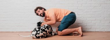 Genç sakallı adam beyaz tuğla karşı Dalmaçyalı köpekli duvar arka plan
