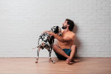 Genç sakallı adam beyaz tuğla karşı Dalmaçyalı köpekli duvar arka plan