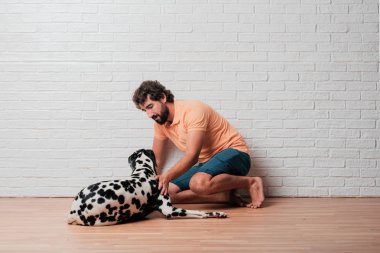 Genç sakallı adam beyaz tuğla karşı Dalmaçyalı köpekli duvar arka plan