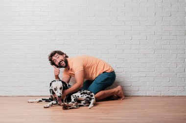 Genç sakallı adam beyaz tuğla karşı Dalmaçyalı köpekli duvar arka plan