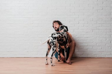 Genç sakallı adam beyaz tuğla karşı Dalmaçyalı köpekli duvar arka plan