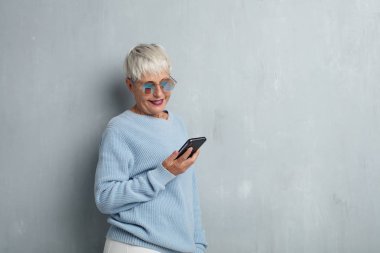 grunge çimento duvara bir akıllı telefon ile cool kadın kıdemli.