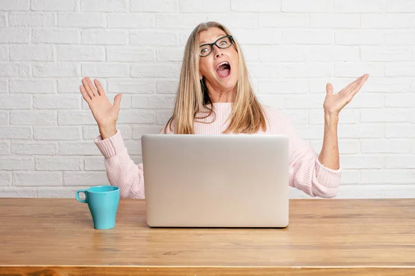 senior businesswoman with a happy surprised expression, eyes wide open and broad smile, with hands on both sides of face showing shock.