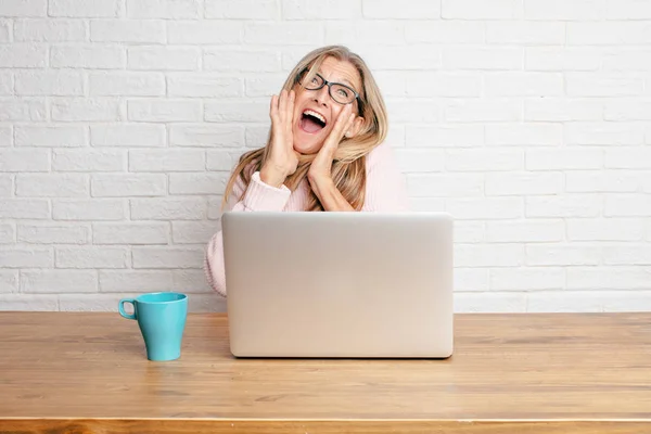 senior businesswoman with a happy surprised expression, eyes wide open and broad smile, holding face with both hands.