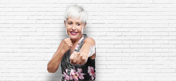 senior cool woman with an angry, aggressive and menacing pose, ready for the fight, showing fists furiously and belligerently.