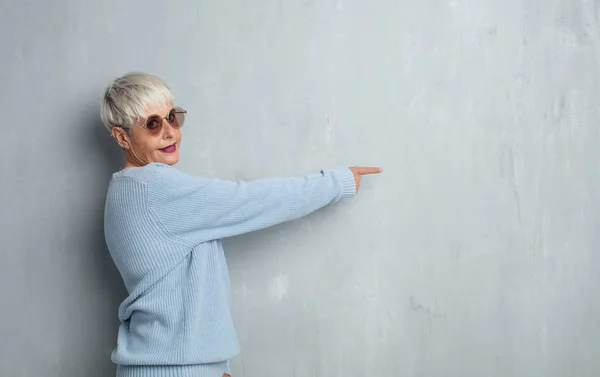 Старша Холодна Жінка Вказує Порожнє Місце Грандж Цементну Стіну — стокове фото
