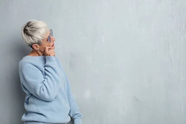 Старшая Холодная Женщина Думает Против Гранж Цементной Стены — стоковое фото