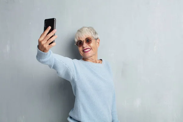 senior cool woman with a smartphone against grunge cement wall.