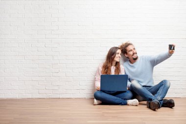 Mutlu genç çift yeni evleri bir dizüstü bilgisayar ile katında oturuyor. Aşk ve ev taşıma kavramı.