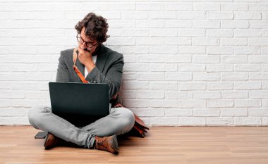 karışık ve düşünceli bir görünüm ile katta oturan, düşünme ve farklı seçenekler arasında merak yana doğru bakarak Genç adam.