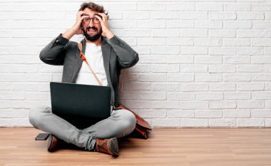 Genç adam bir deli ile katta oturan hayran sürpriz, görünümünü saç çekerek kafa iki eliyle tutarak.