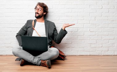 bir nesne veya kavramı tek elle ve diğer el ile kalça üzerinde gösterilen memnun bir ifade ile gülümseyen katta oturan genç adam.