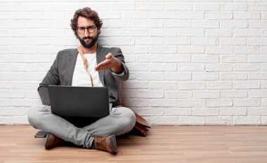 Genç adam ciddi bir zemin üzerinde oturan kendine güvenen, gurur ve sert ifade bir anlaşma kapanış bir el sıkışma sunan veya tebrik ve sizi karşılayan.