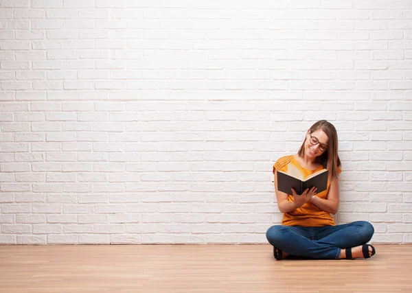年轻漂亮的女人读一本书坐在木地板上对砖墙纹理 — 图库照片