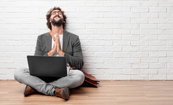 young man sitting on the floor praying in a saintly manner, begging "please" for a wish to happen.