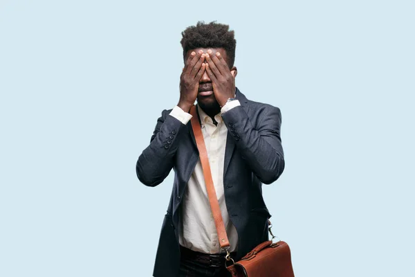young black businessman with a serious, scared, frightened expression, covering eyes with both hands.