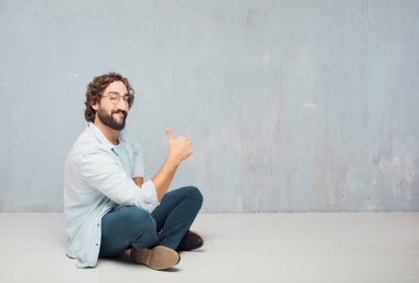 Genç serin sakallı adam yere oturma. Grunge duvar arka plan.