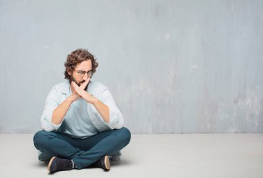 Genç serin sakallı adam yere oturma. Grunge duvar arka plan.