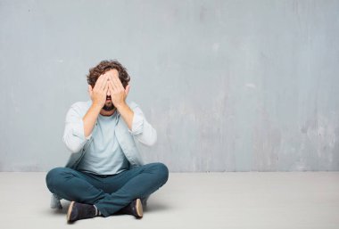 Genç serin sakallı adam yere oturma. Grunge duvar arka plan.