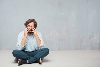 Genç serin sakallı adam yere oturma. Grunge duvar arka plan.