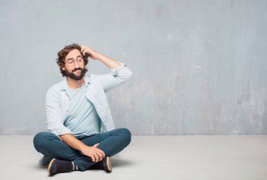 Genç serin sakallı adam yere oturma. Grunge duvar arka plan.