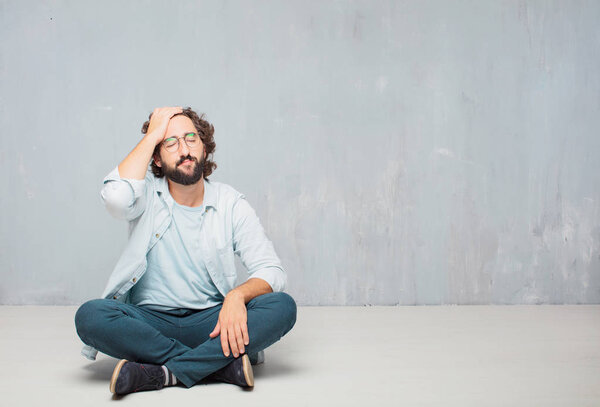 Young cool bearded man sitting on the floor. Grunge wall background.