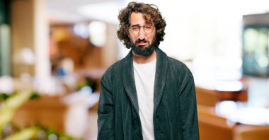 Bornoz giyen genç adam üzgün bir şekilde gece elbisesi giyiyor.