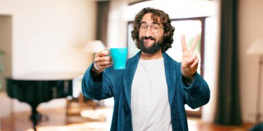 Bornoz giyen genç adam kahve içiyor.