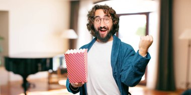 Bornoz giyip, üzerinde patlamış mısır kovası olan genç adam.