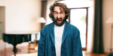 Bornoz giyen genç adam kızgın bir poz veriyor.