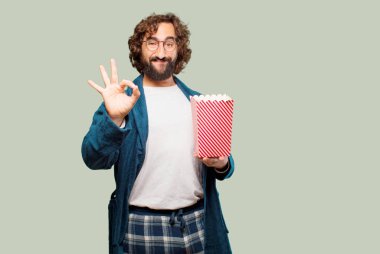 Bornoz giyip, üzerinde patlamış mısır kovası olan genç adam.