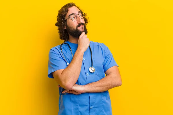 Młody pielęgniarka człowiek myśli przeciwko żółtym tle — Zdjęcie stockowe