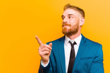 genç kırmızı baş işadamı mutlu gülümseyerek ve yan lara bakarak, merak, düşünme veya turuncu arka plan karşı bir fikir sahip