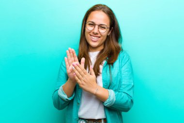 mutlu ve başarılı, gülümseyen ve el çırpan genç kadın, mavi arka plan karşı bir alkış ile tebrik söyleyerek