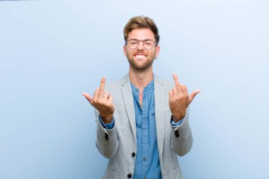 young businessman feeling provocative, aggressive and obscene, flipping the middle finger, with a rebellious attitude against blue background