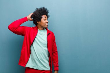 Genç siyah sporcu şaşkın ve kafası karışmış hissediyor, başını kaşıyor ve grunge duvarına bakıyor.