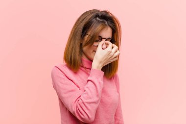 young pretty woman feeling stressed, unhappy and frustrated, touching forehead and suffering migraine of severe headache against pink background