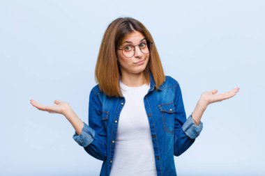 Genç, güzel bir kadın şaşkın ve şaşkın, şüpheci, farklı seçenekleri tartıyor ya da seçiyor. Mavi arka planda komik bir ifade var.