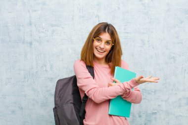 Genç bayan öğrenci neşeyle gülümsüyor, mutlu hissediyor ve bir konsepti fotokopi odasında gösteriyor. Avuç içi grunge duvar arkası ile.
