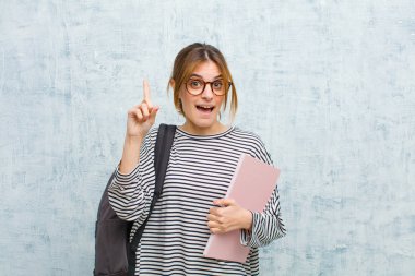 Genç bayan öğrenci bir fikri fark ettikten sonra mutlu ve heyecanlı bir dahi gibi hissediyor, neşeli bir şekilde parmağını kaldırıyor, eureka! grunge duvar arka planına karşı