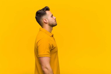 Profil görünümlü genç İspanyol adam uzayı kopyalamaya çalışıyor, düşünüyor, hayal ediyor ya da turuncu duvara karşı hayal kuruyor.