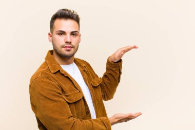 Genç İspanyol bir adam iki eliyle fotokopi alanında bir nesneyi tutuyor, izole edilmiş arka plana karşı bir nesneyi gösteriyor, sunuyor ya da reklamını yapıyor.