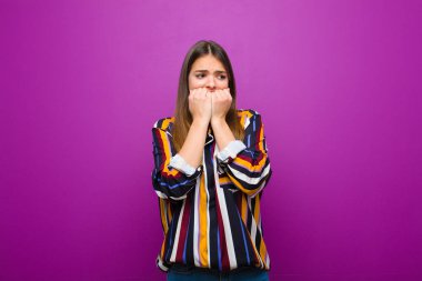 Genç, güzel bir kadın endişeli, gergin, stresli ve korkmuş görünüyor. Tırnaklarını yiyor ve mor arka plana karşı yanal fotokopi alanı arıyor.