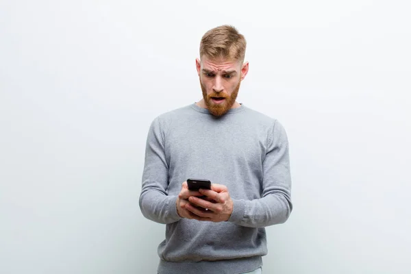白い背景に対してスマートフォンを持つ若い赤い頭の男 — ストック写真