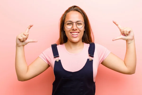 young  woman framing or outlining own smile with both hands, looking positive and happy, wellness concept against pink background