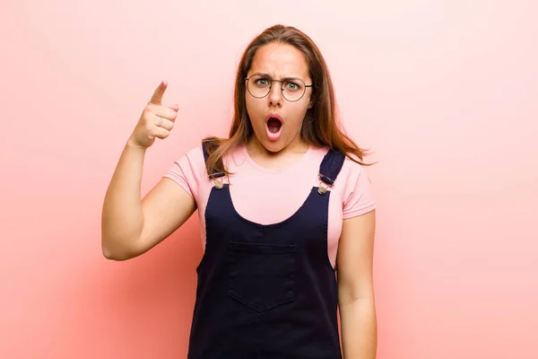 young  woman pointing at camera with an angry aggressive expression looking like a furious, crazy boss against pink background