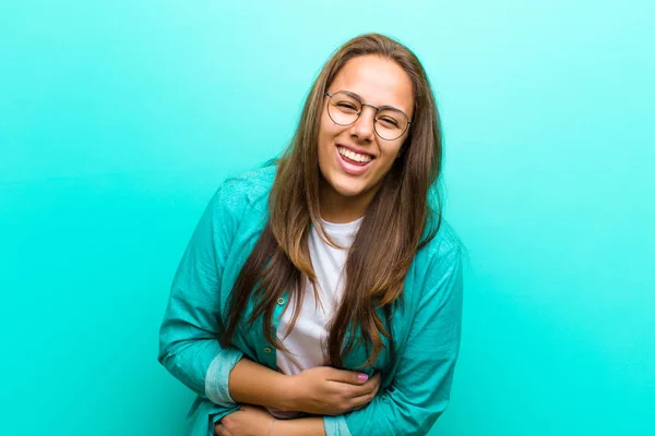 young woman laughing out loud at some hilarious joke, feeling happy and cheerful, having fun against blue background